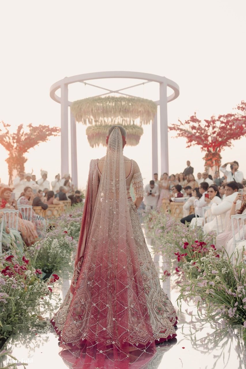 Photo of Stunning back shot of the bride in a ombre dupatta as she walks down the aisle towards the mandap