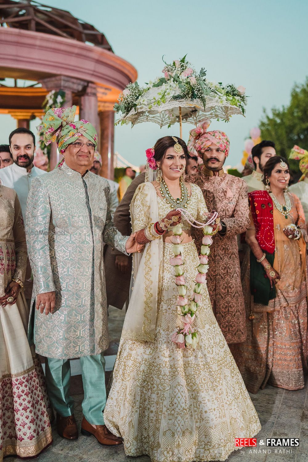 Photo of A bride in an ivory and gold lehenga under a floral umbrella for her wedding