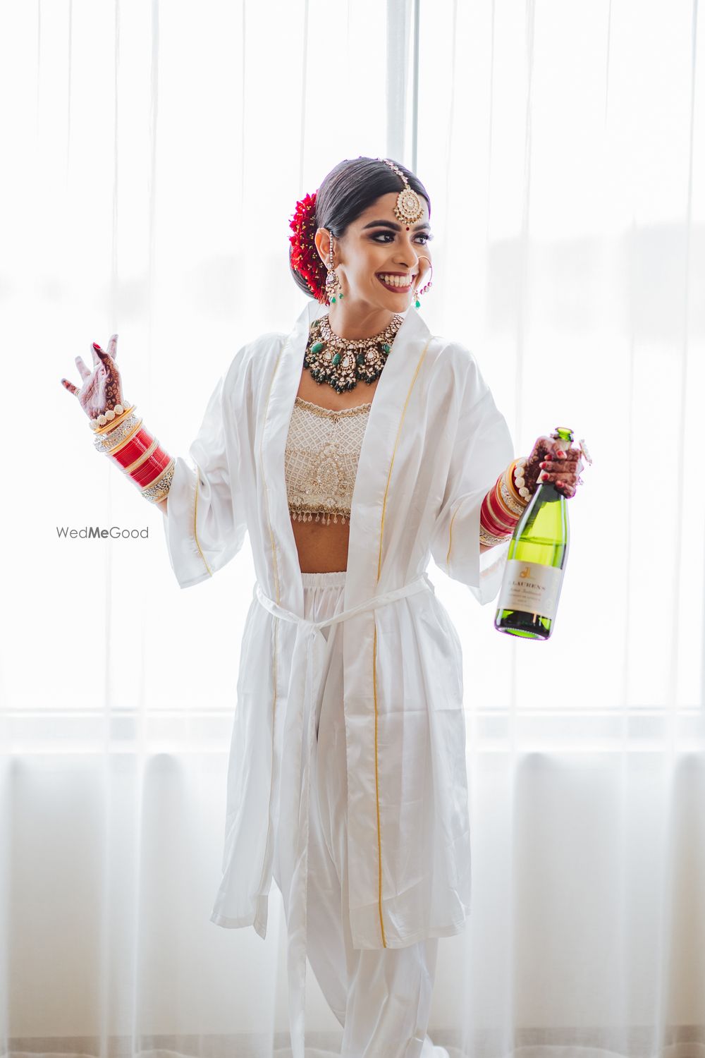 Photo of bride wearing a robe holding a champagne getting ready shot