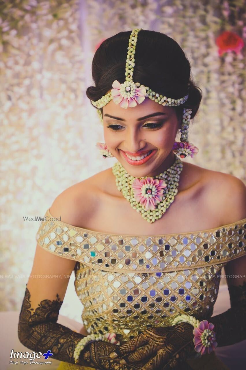 Photo of A to-be-bride in an off-shoulder top and floral jewellery on her mehndi ceremony