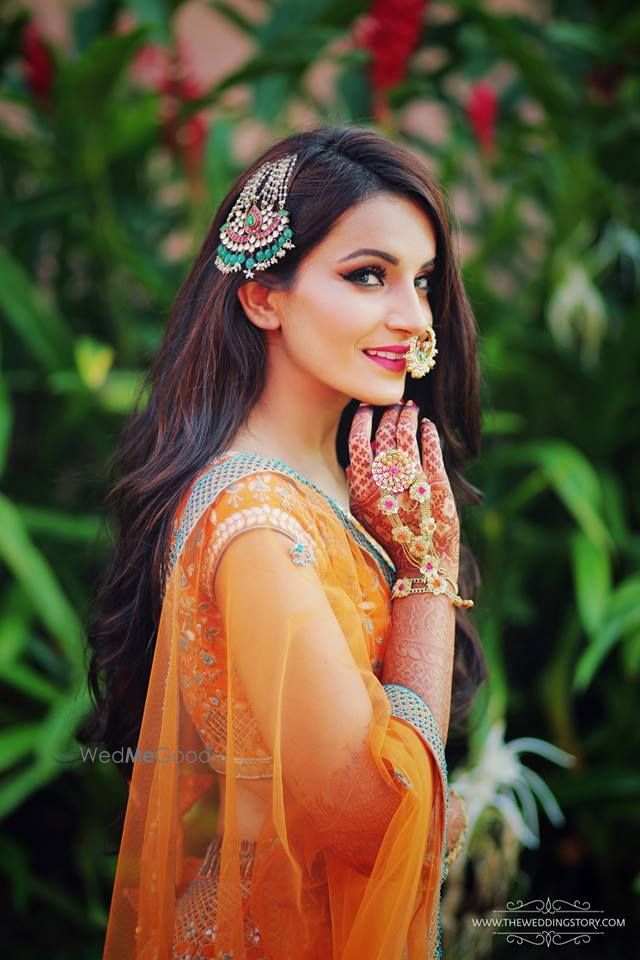 Photo of Bride in orange mehendi lehenga and unique jewellery