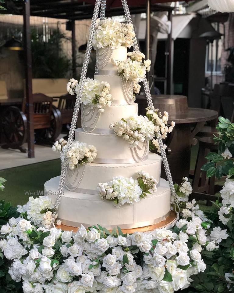 Photo of White wedding cake on a swing with florals