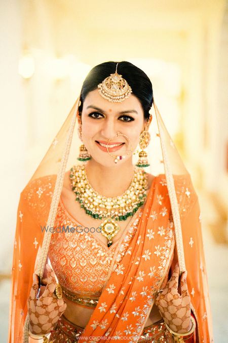 Photo of A bride in orange with gold and turquoise jewellery poses for the camera.