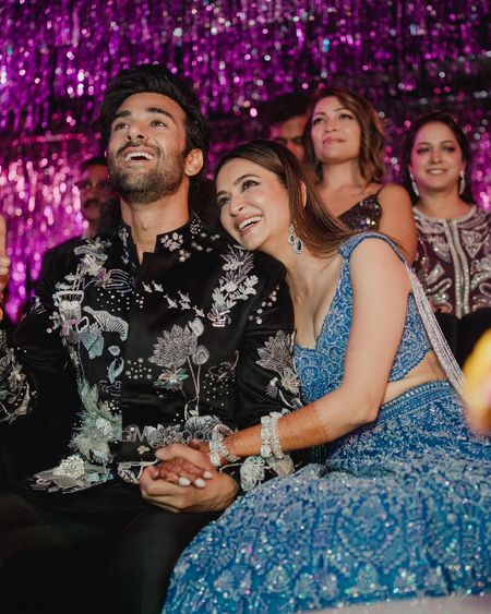 Photo of Sangeet shot of the bride and groom with the groom in a botanical work sherwani and bride in a cerulean blue lehenga