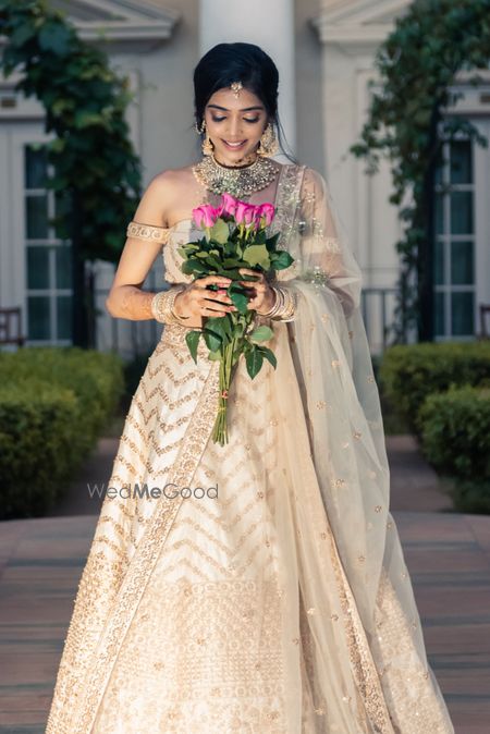 Photo of A bride in an ivory and gold lehenga with off-shoulder blouse and gold jewellery