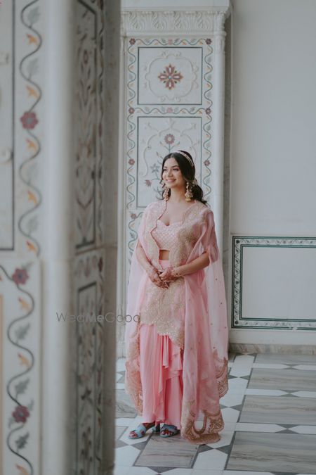 Photo of Gorgeous powder pink outfit for haldi with a jacket style cape and lovely sispatti for the bride