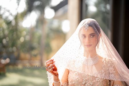 Photo of Lovely veil shot of the bride in a lace and shimmer pastel peach lehenga