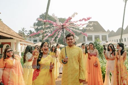 Photo of couple entering under floral umbrella for their haldi