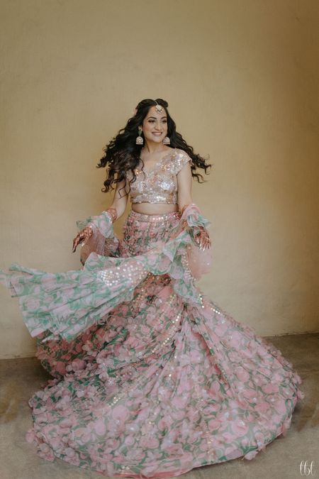 Photo of bride twirling in light pink mehendi lehenga with ruffled dupatta