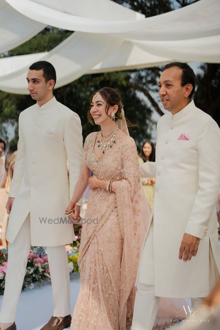 Photo of Happy candid capture of the bride entering the mandap with her brother and father, all in pastel outfits