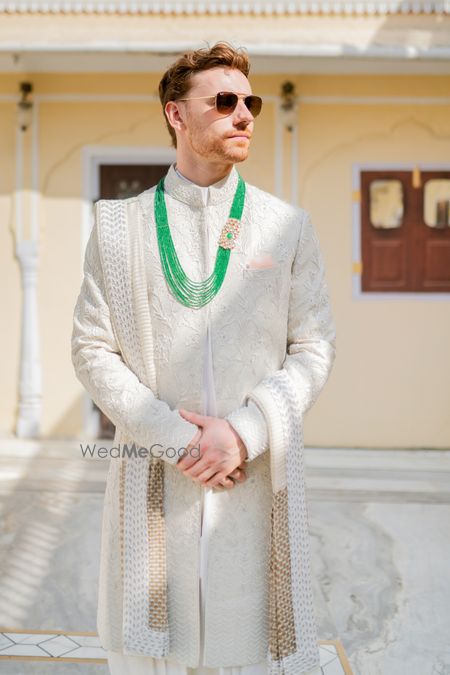 Photo of groom in ivory sherwani with green jewellery