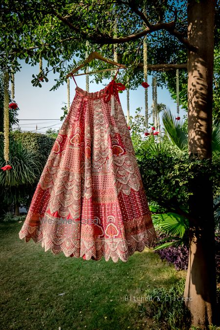 Photo of Bridal lehenga in red and white hues, hung on hangar