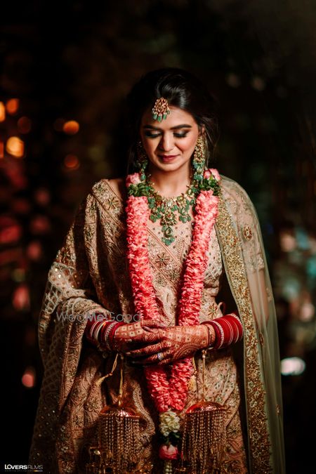 Photo of Bride wearing a pastel pink lehenga with emerald jewellery.