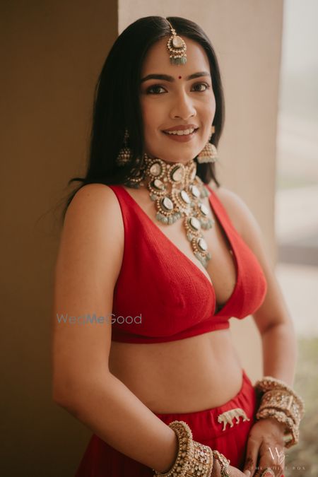 Photo of Gorgeous bridal portrait with a statement necklace and jhumkis along with a plunge neck blouse in all red