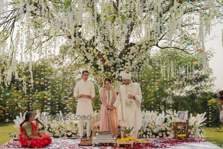 Photo of Gorgeous tree mandap with white florals as the couple takes pheras in an outdoor wedding