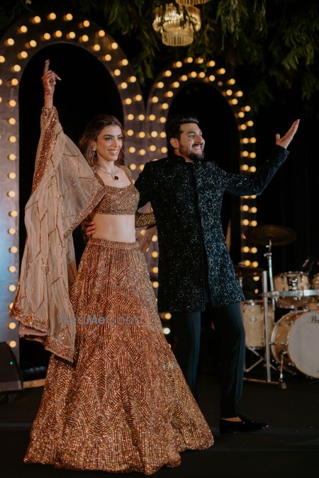 Photo of Candid capture of the bride and groom as they take on the stage in a champagne gold lehenga and black sherwani