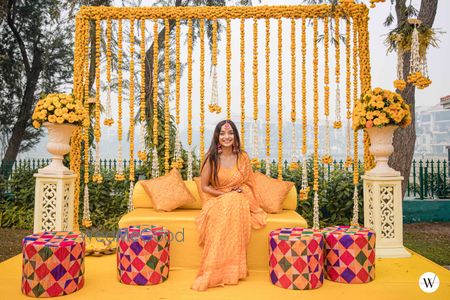 Photo of bride in yellow saree against pretty haldi backdrop