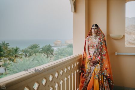 Photo of unique bridal lehenga in orange with matching chuda