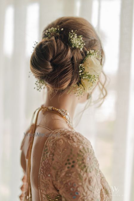 Photo of Soft and twisted bridal bun wedding hairdo with white roses and baby breath