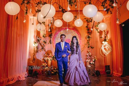 Photo of A bride in a gown and a groom in a blue suit enter together for their sangeet/cocktail function.