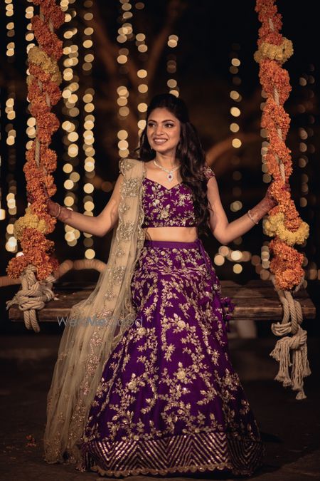 Photo of Bride in an aubergine coloured lehenga sitting on Jhoola.