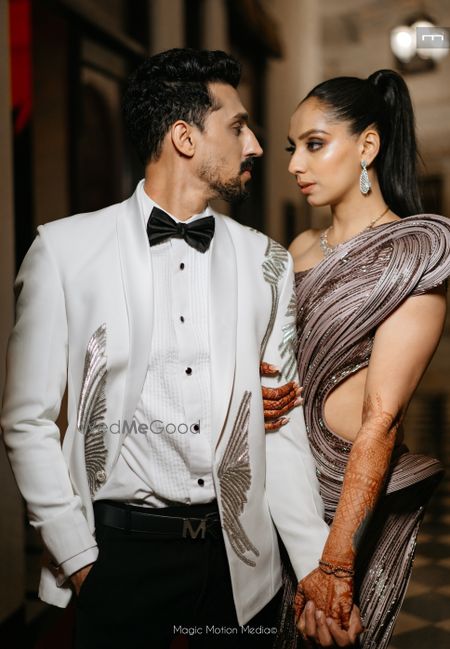 Photo of Fun shot of the couple with the groom in a white tuxedo and bride in a modern shimmery gown