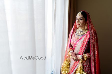 Photo of A bride in a red lehenga with gold kalire posing on her wedding day