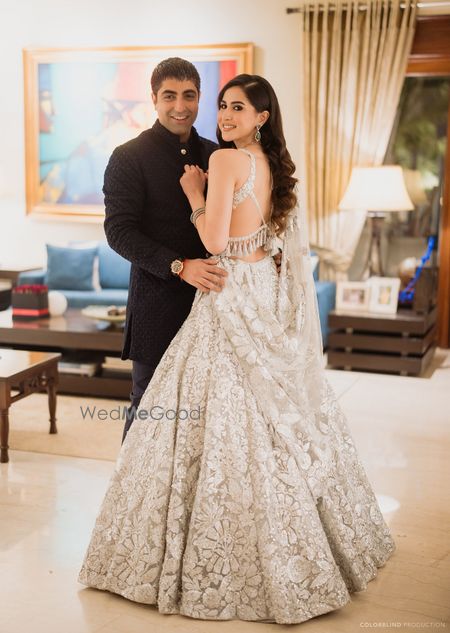 Photo of Gorgeous white lehenga with open hairstyle on the sangeet night with a cutout backless blouse and the groom in a black ensemble