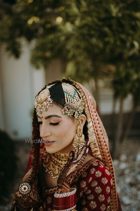 Photo of contrasting bridal jewellery with red sabyasachi lehenga including passa