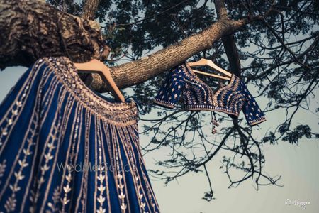 Photo of Dark blue lehenga and blouse on hanger hanging on tree