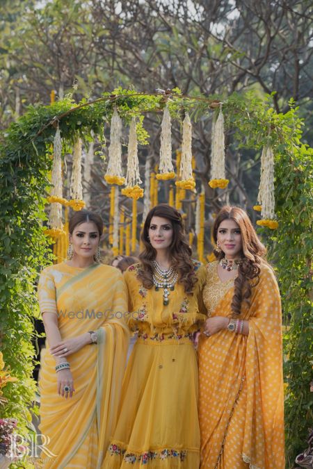 Photo of bride and her sisters in matching yellow outfits on mehendi