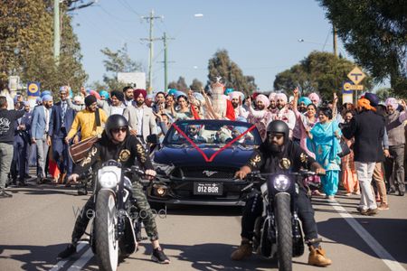 Photo of A groom enters on a vintage car with a bike entourage