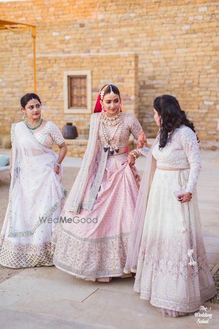 Photo of bride in a light pink lehenga with her bridesmaids matching in white