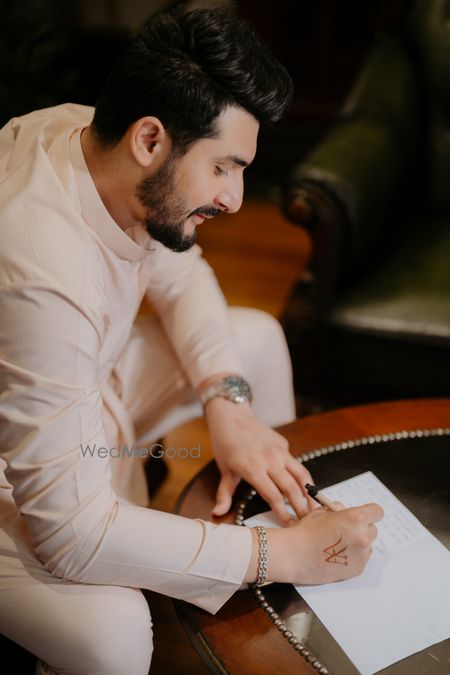 Photo of A groom to be writing his vows and a love letter to the bride to be in a peach sherwani