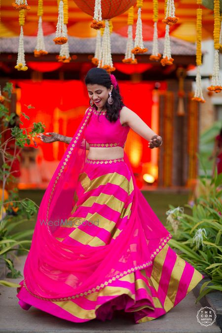 Photo of Bride twirling on mehendi in bright pink and lime green lehenga