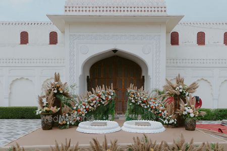 Photo of Outdoor haldi setup with fresh and dry floral arrangements and white urlis