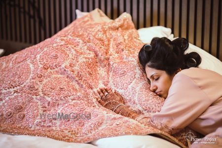 Photo of bride hugging her lehenga and sleeping getting ready shot