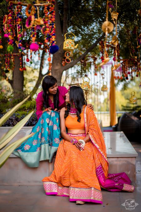 Photo of Bride sitting with bridesmaid on mehendi