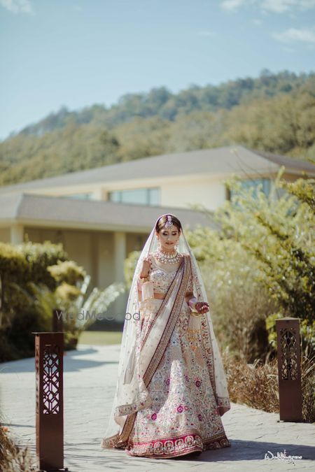 Photo of wedding day bridal portrait outdoors in a white lehenga