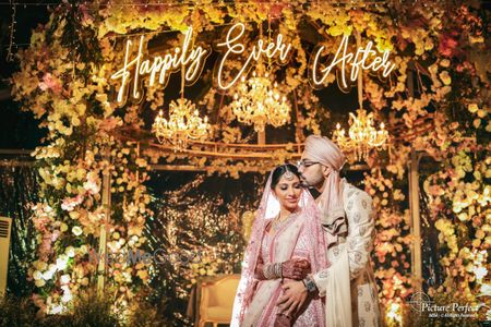 Photo of A candid shot of the couple in pastel outfits with Happily Ever After backdrop.