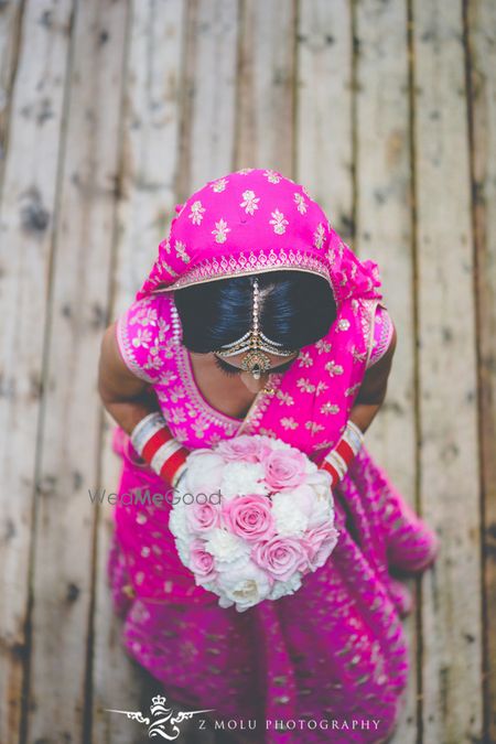 Photo of Bride in bright pink lehenga holding bridal bouquet