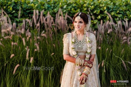 Photo of A bride in an ivory and gold lehenga with pastel jaimala