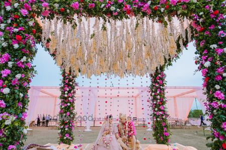 Photo of The bride and groom under a gorgeous floral mandap.