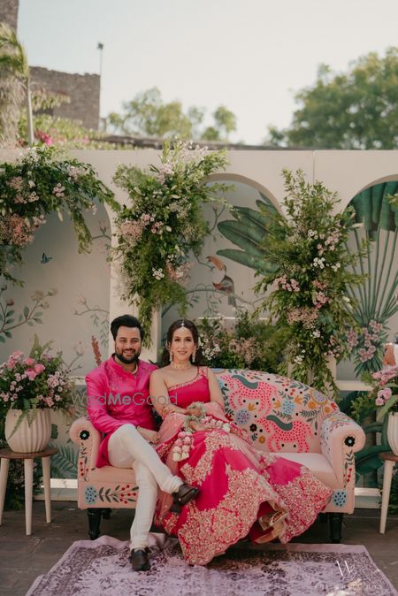 Photo of Pretty shot of the couple sitting on a printed sofa with coordinated hot pink outfits