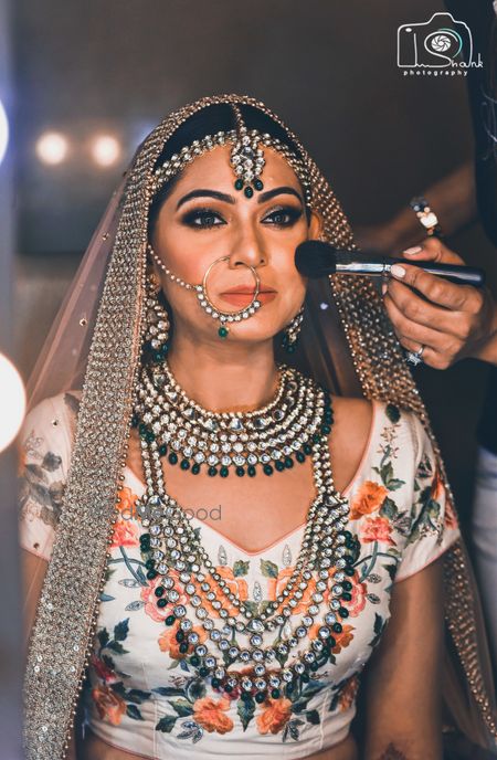 Photo of Bride in floral lehenga getting makeup done