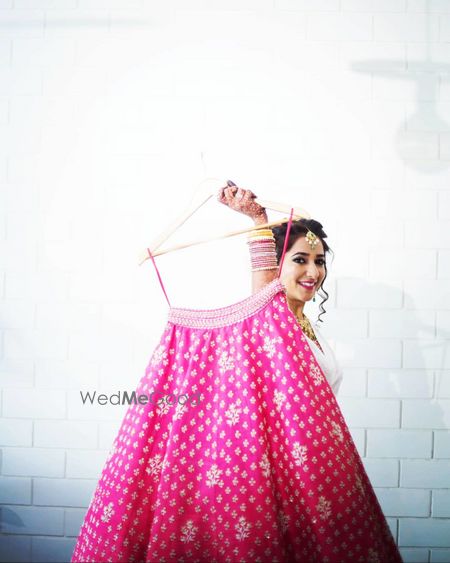 Photo of bride getting ready shot holding up her pink lehenga