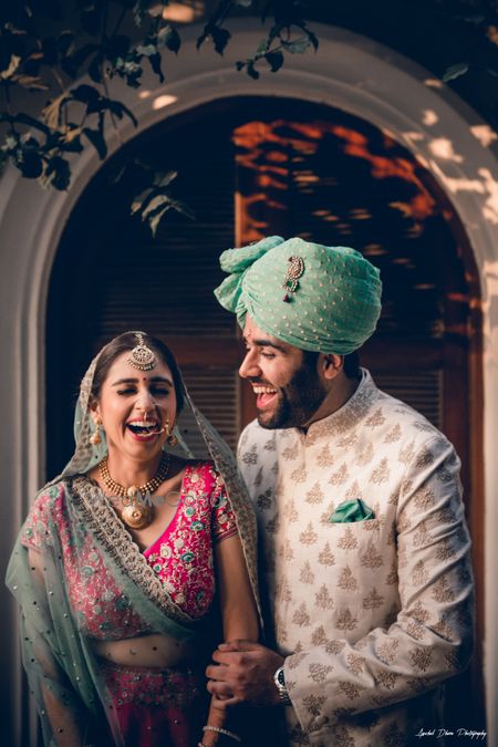 Photo of A bride and groom in color-coordinated outfits laughing on their wedding day