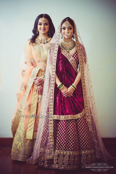 Photo of Bride with sister wearing maroon bridal lehenga