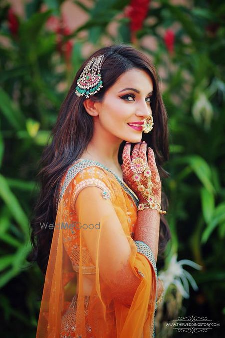 Photo of Bride in orange mehendi lehenga and unique jewellery