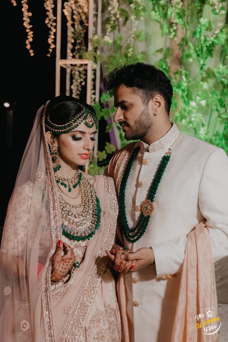 Photo of Pastel bride and groom outfits with dark green contrasting necklaces